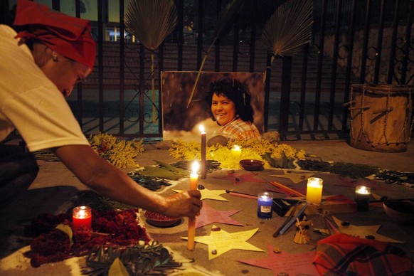 A woman places a candle in front of a picture of murdered environmental activist Berta Caceres, as people perform a ritual for her outside the Supreme Court in Tegucigalpa, Honduras, Sunday, Sept. 16, ...