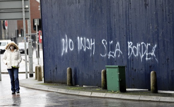 FILE - In this Wednesday, Feb. 3, 2021 file photo, a woman walks past past graffiti with the words &#039;No Irish Sea Border&#039; in Belfast city centre, Northern Ireland. The schism of Brexit has cr ...