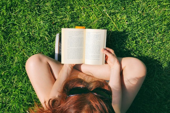 Lovely young woman sitting on the grass in park and reading the book, enjoying life with no technology involved.