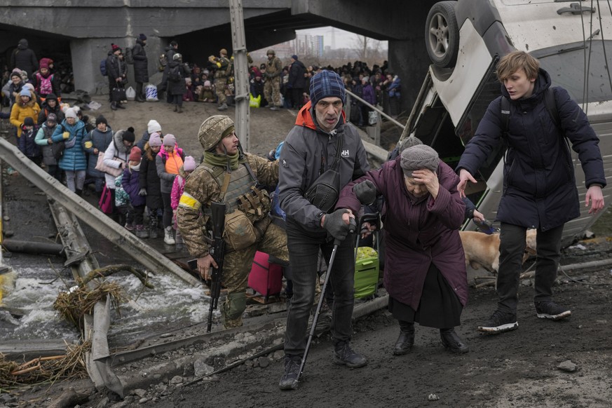 An elderly lady is assisted while crossing the Irpin river, under a bridge that was destroyed by a Russian airstrike, as civilians flee the town of Irpin, Ukraine, Saturday, March 5, 2022. What looked ...