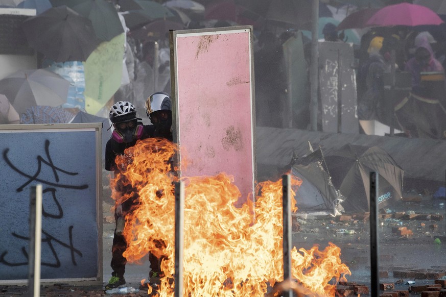 Protestors look out from behind a barricade as a fire burns near Hong Kong Polytechnic University in Hong Kong, Sunday, Nov. 17, 2019. A Hong Kong police officer was hit in the leg by an arrow Sunday  ...