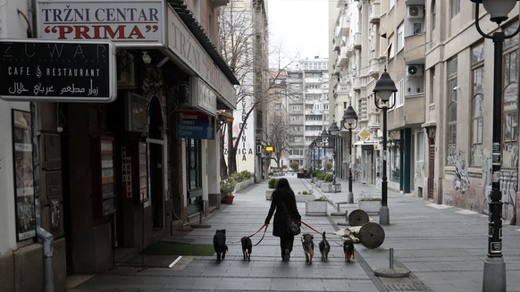 A woman walks with dogs in a deserted street amid the coronavirus outbreak in downtown Belgrade, Serbia, Thursday, March 26, 2020. The new coronavirus causes mild or moderate symptoms for some people, ...