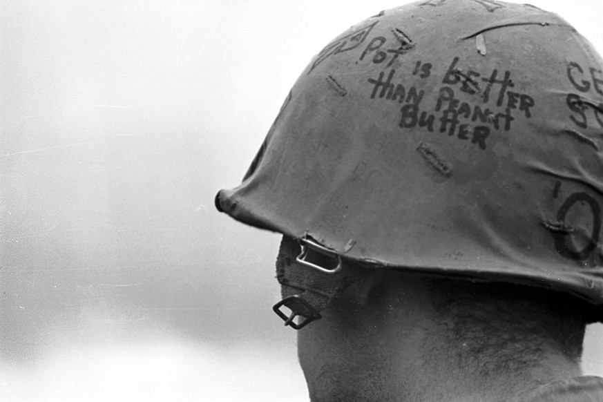 (Original Caption) A soldier in Vietnam is shown wearing a helmet with the slogan "Pot is better than peanut Butter."