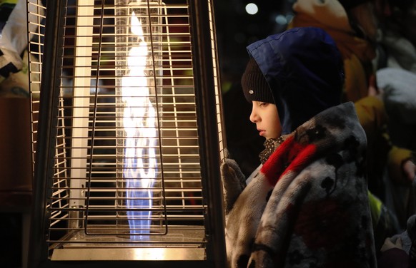 epa09806536 A Ukrainian refugee boy, who wears a blanket on his shoulders, warms-up near a burning gas heater shortly after passing through the border crossing of Siret, northern Romania, 06 March 202 ...