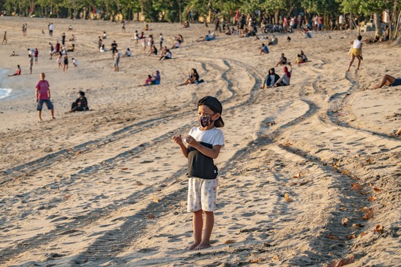 epa08559729 A boy wearing a protective face mask plays on Kuta Beach amid coronavirus pandemic in Kuta, Bali, Indonesia, 03 July 2020. (issued 22 July 2020) The country reported its first case of COVI ...
