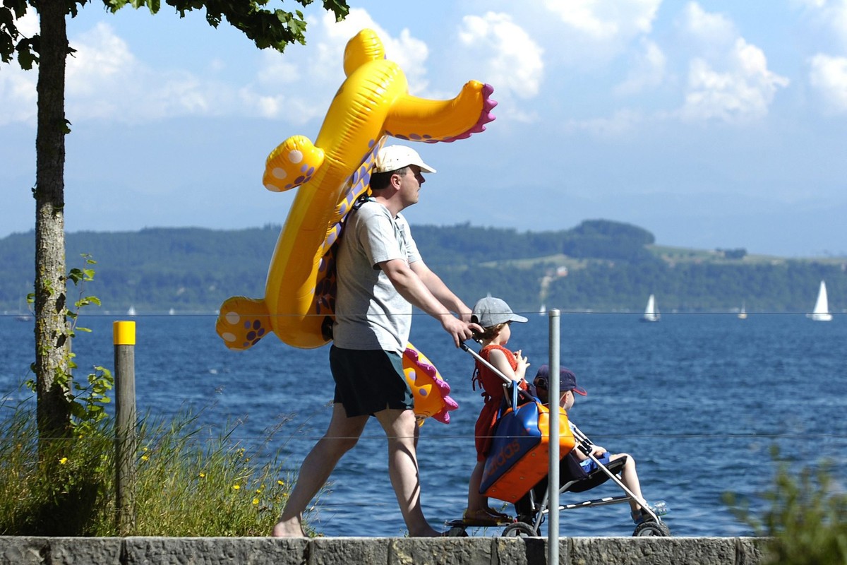 Une famille rentre de la plage d'Auvernier NE, ce dimanche 19 juin 2005, avec un petit bateau pneumatique en forme de dragon pour enfant, porte par le papa. Les temperatures estivales ont favoris ...