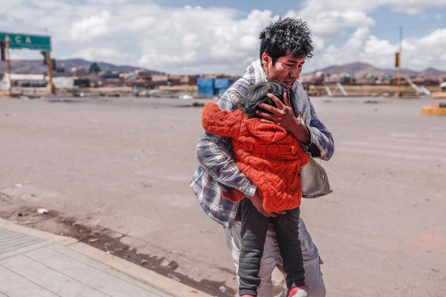 epa10394496 A man shields a child as he runs for cover during the protests in the vicinity of the Juliaca airport, in Juliaca, Peru, 07 January 2022. Protest demonstrations against the government of D ...