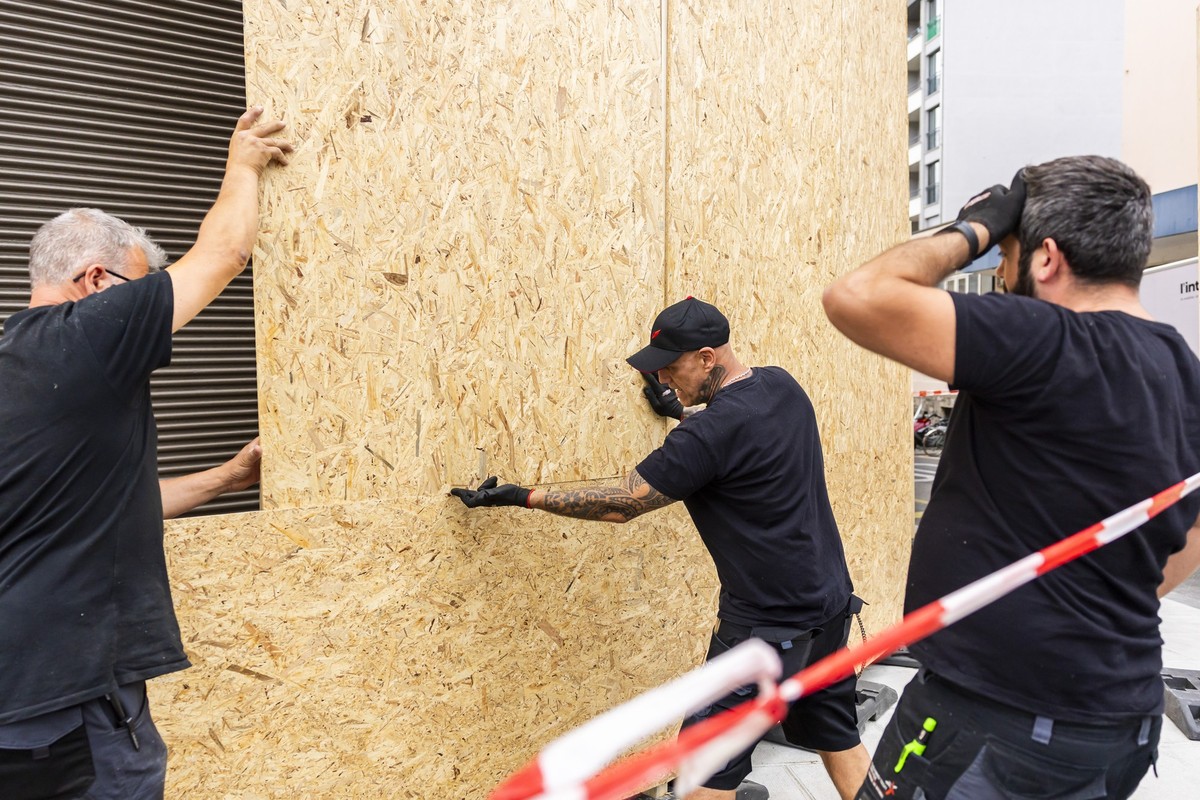 Des ouvriers installent des planches de bois devant les vitrines d'un etablissement pour le proteger d'eventuelles degradations de la part de manifestants durant la manifestation NoG7 liee a ...