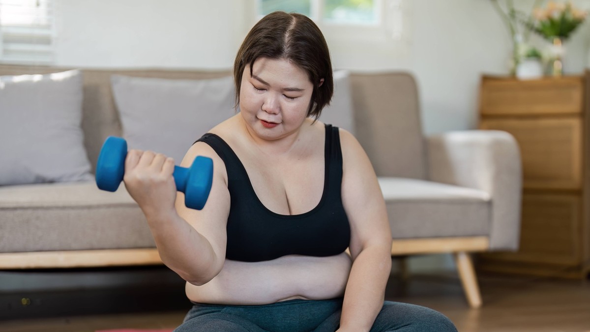 Confident Overweight Woman Exercising at Home with Dumbbells for a Healthy Lifestyle and Fitness Routine Overweight woman exercising at home with dumbbells, promoting a healthy lifestyle and fitness., ...