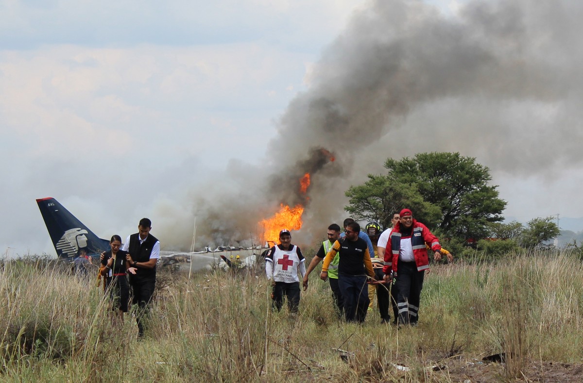 In this photo released by Red Cross Durango communications office, Red Cross workers and rescue workers carry an injured person on a stretcher, right, as airline workers, left, walk away from the site ...