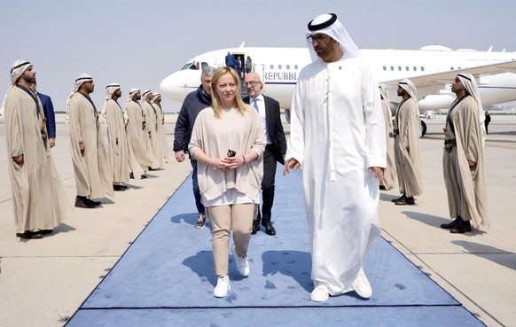 epa10500410 A handout photo made available by Chigi Palace Press Office shows Italian Prime Minister Giorgia Meloni (C) being welcomed by United Arab Emirates Minister of Industry and Advanced Technol ...