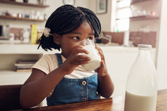 Black child, drink and milk in home for nutrition, hygiene and dental health in kitchen table. Family house, girl and glass of dairy product for wellness, protein and vitamins for growth for kid Black ...