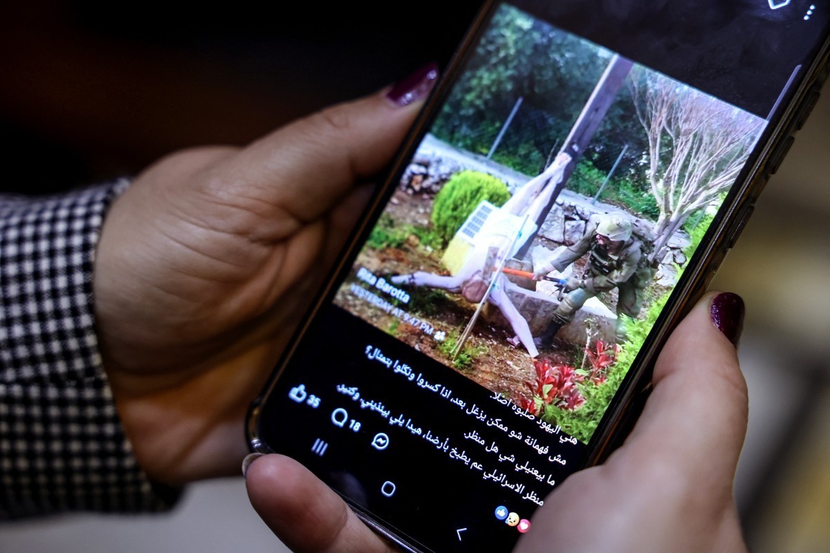 A woman checks a social media post on her mobile phone featuring an image that appears to show an Israeli soldier hitting a statue of Jesus Christ in the southern Lebanese Christian village of Debl, i ...