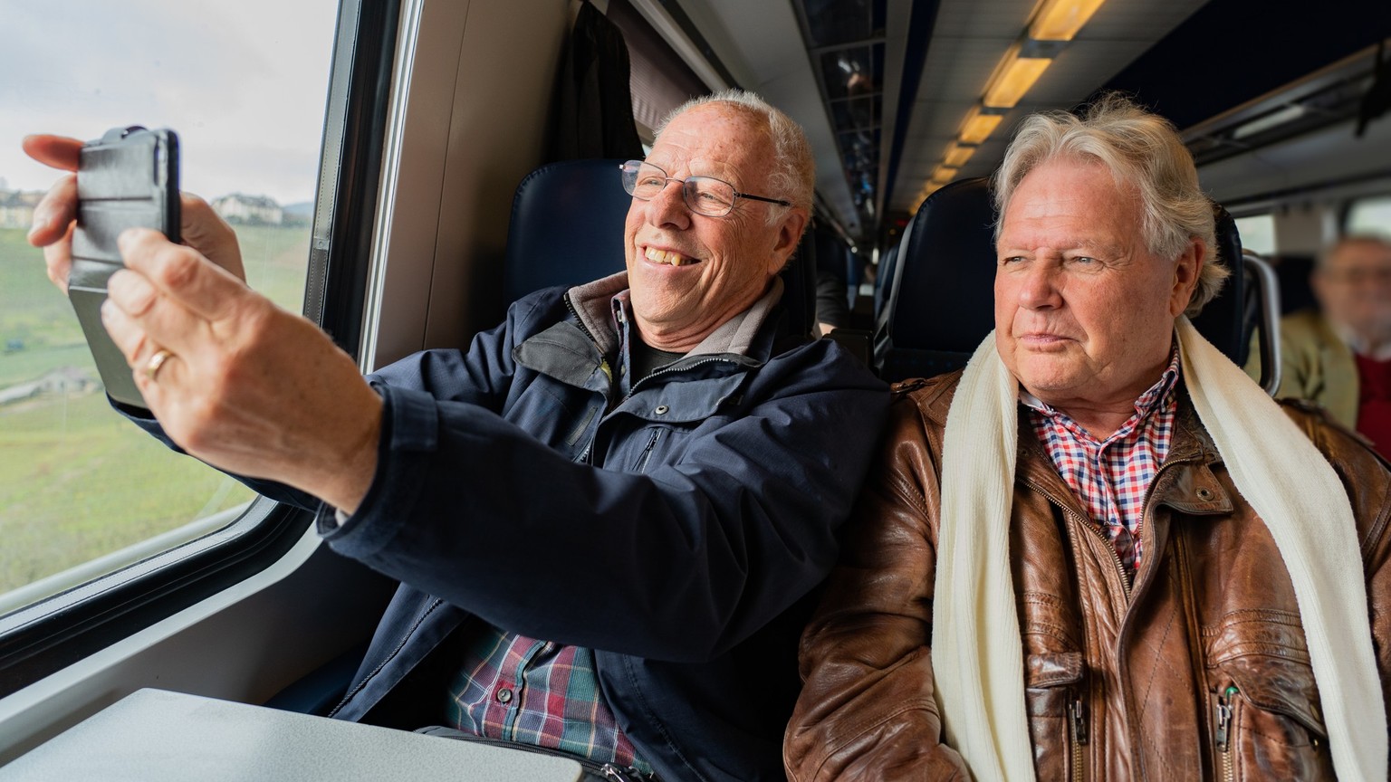 Older man with a good friend in casual wear is taking a self portrait with a smart phone in train in Switzerland at daylight. Model Released Property Released xkwx {pensioner,portrait,person,adult,eld ...