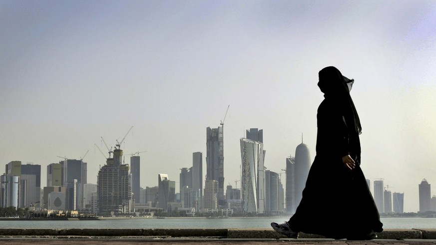 FILE- A Qatari woman walks in front of the city skyline in Doha, Qatar on May 14, 2010. After FIFA awarded the World Cup to Qatar, there were questions about what women would be allowed to wear. The l ...