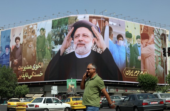 epa12115837 An Iranian man walks next to a huge poster of late Iranian President Ebrahim Raisi displayed for his death anniversary, at the Enqelab square in Tehran, Iran, 19 May 2025. Iranian Foreign  ...