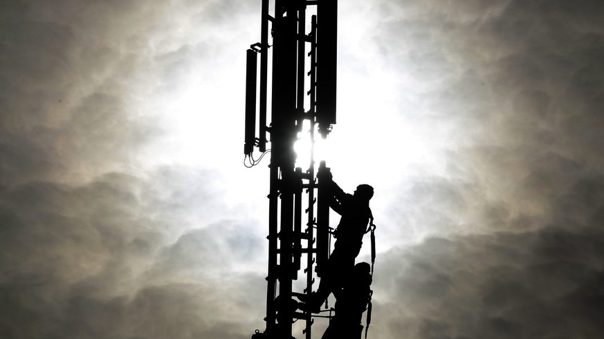 Two workers are silhouetted as they fix a mobile phone pole against the sun in Duisburg, western Germany, Tuesday Oct.26,2010. The advanced use of mobile data with 3 G and the for the future planned 4 ...