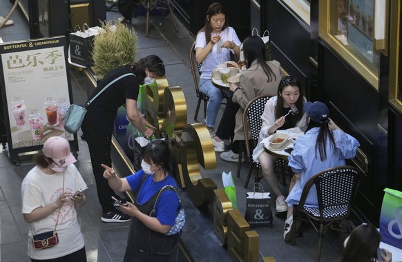 Women, lower left, wearing face masks chat each other as people eat at a reopened restaurant in a shopping mall in Beijing Monday, June 6, 2022. Diners returned to restaurants in most of Beijing for t ...
