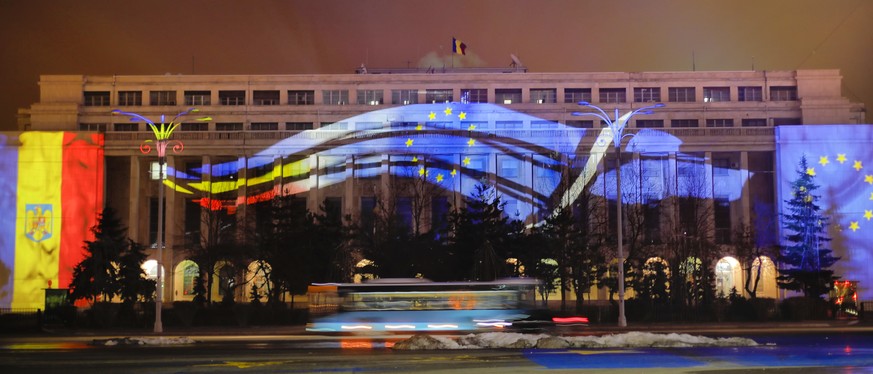 In this Sunday, Dec. 30, 2018, photo European Union and Romanian flags are projected on the Victoria palace, the Romanian government headquarters in Bucharest, Romania, two days before the country wil ...