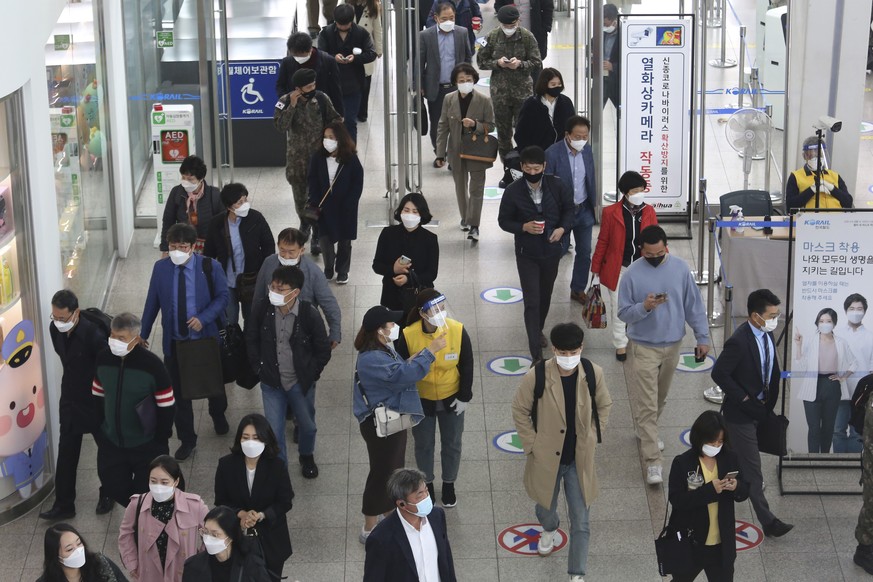 An employee, center right, wearing a face mask and face shield to help protect against the spread of the coronavirus, guides a passenger at the Seoul Railway Station in Seoul, South Korea, Thursday, O ...