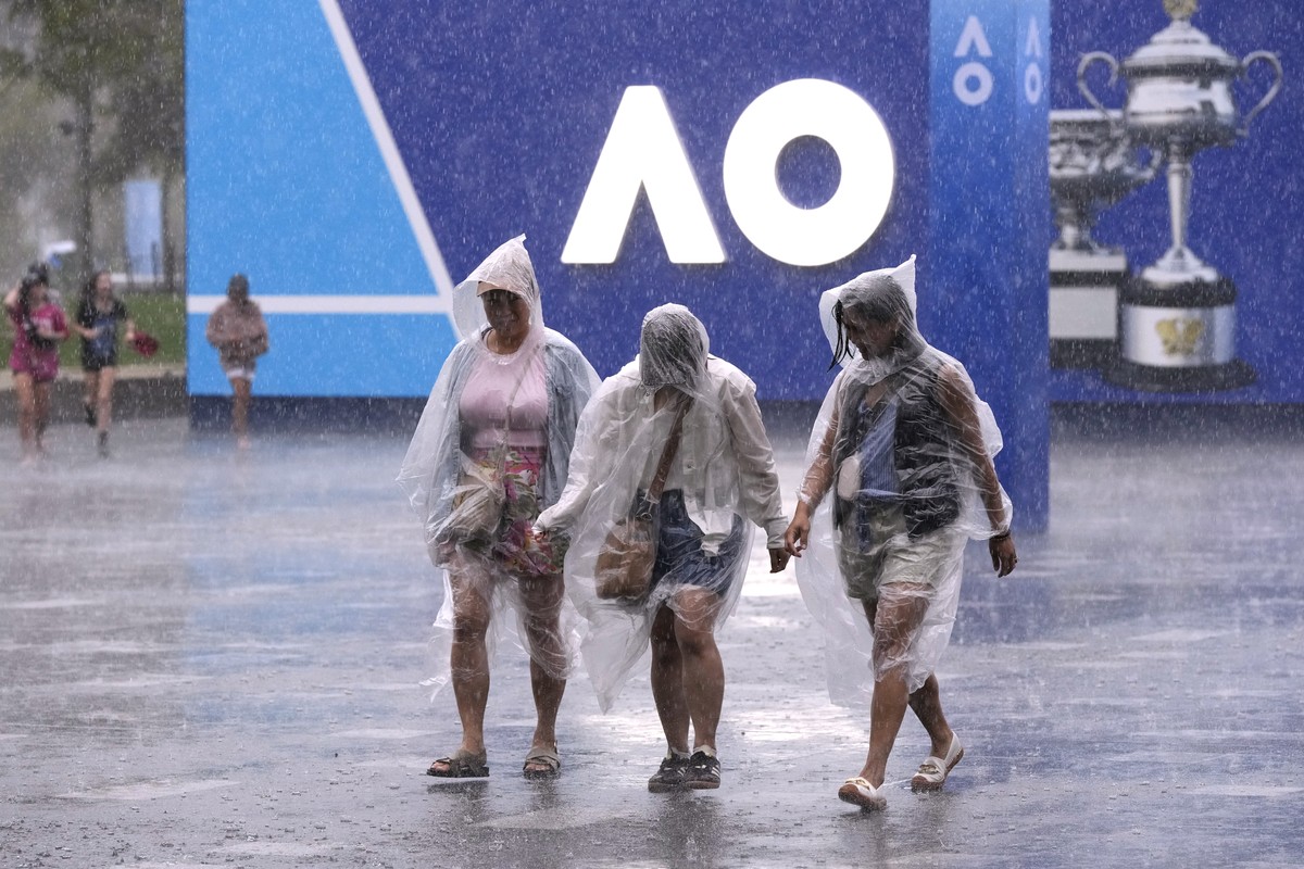 Spectators walk through the rain as play is suspended during first round matches at the Australian Open tennis championship in Melbourne, Australia, Sunday, Jan. 12, 2025. (AP Photo/Manish Swarup)