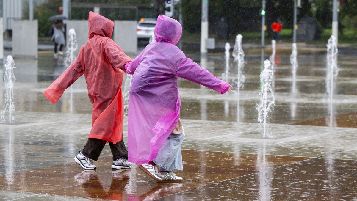 Des touristes se promenent avec leurs pelerine sous la pluie et face aux jets de la fontaine de la place des Nations, ce jeudi 26 septembre 2024 a Geneve. Meteo Suisse annonce une alerte de niveau tro ...