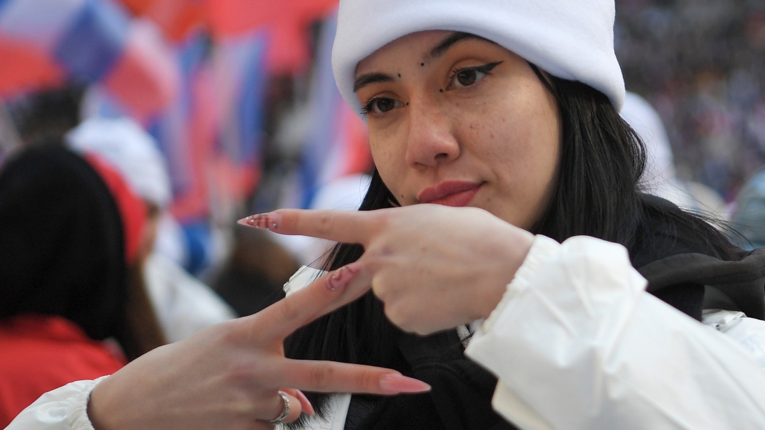 A young woman shows the letter Z, which has become a symbol of the Russian army, and reads a hashtag "We won't let ours down" while other people with Russian national flags gather to join…