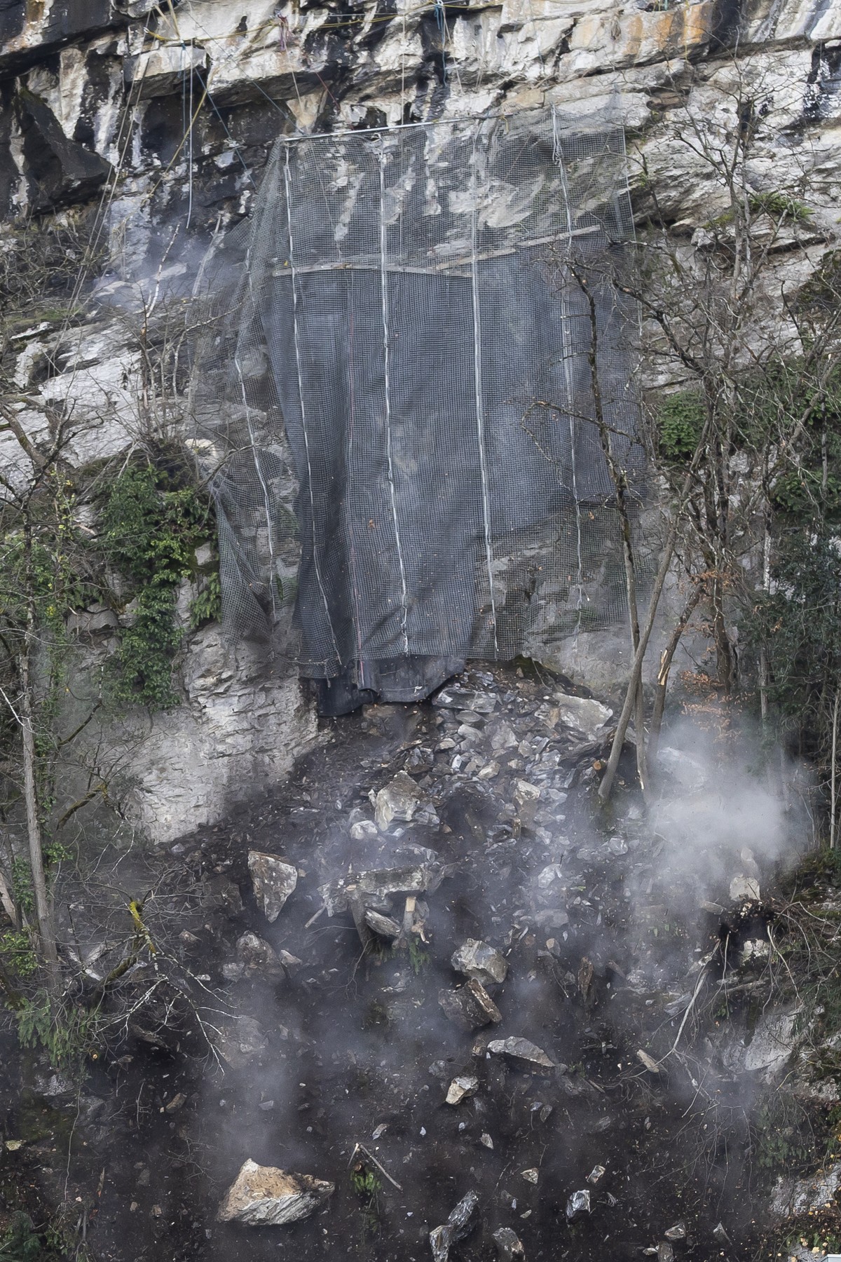 Des blocs de pierre et de la terre tombent de la paroi lors du minage d'un bloc rocheux de la falaise de la Barme ce mardi 2 decembre 2025 a Collombey-Muraz. (KEYSTONE/Cyril Zingaro)
