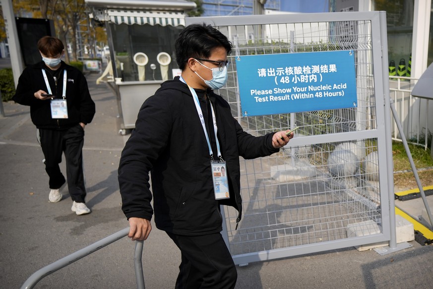 Workers wearing face masks to protect against COVID-19 walk past a sign reminding visitors to show proof of a negative coronavirus test within the past 48 hours to enter the Beijing National Aquatics  ...