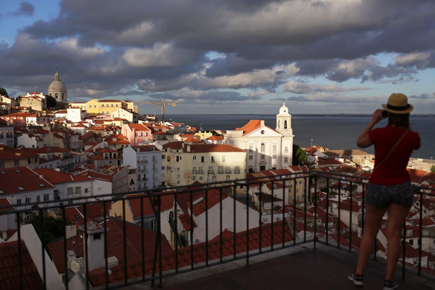 A young woman takes a picture of Lisbon&#039;s Alfama neighborhood from a viewpoint above it at sunset Saturday, Aug. 15 2015. The river facing hillside of Alfama, with its maze of tiny streets, dead  ...