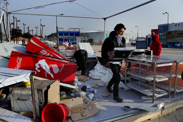 A concession stand worker carries away equipment after strong winds tore apart the food stand at Gangneung Olympic Park at the 2018 Winter Olympics in Gangneung, South Korea, Wednesday, Feb. 14, 2018. ...