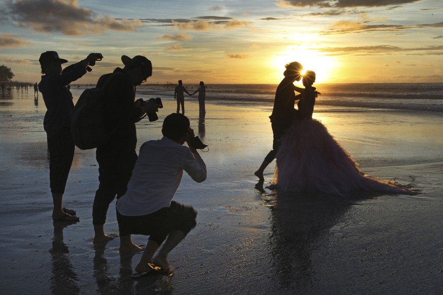 FILE- In this Jan. 18, 2017, file photo, photographers take photos of a tourist couple&#039;s wedding at the famous Kuta beach during sunset in Bali, Indonesia. According to a 2016 survey from wedding ...