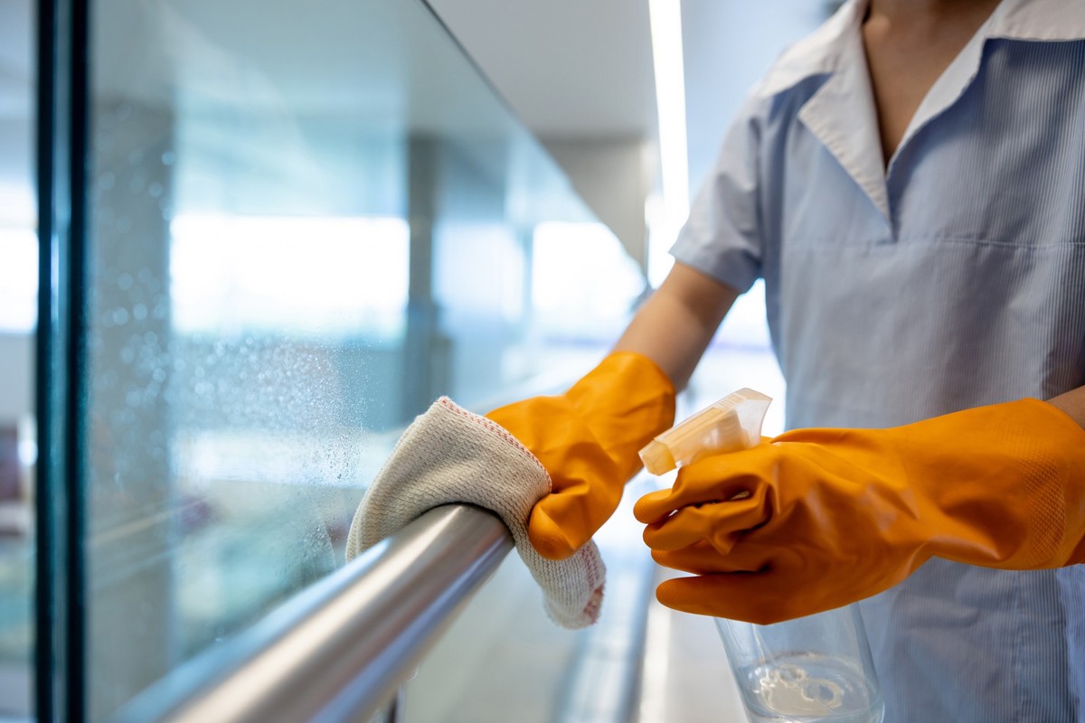 Close-up on a cleaner working at a hospital and cleaning a handrail - janitorial service concepts