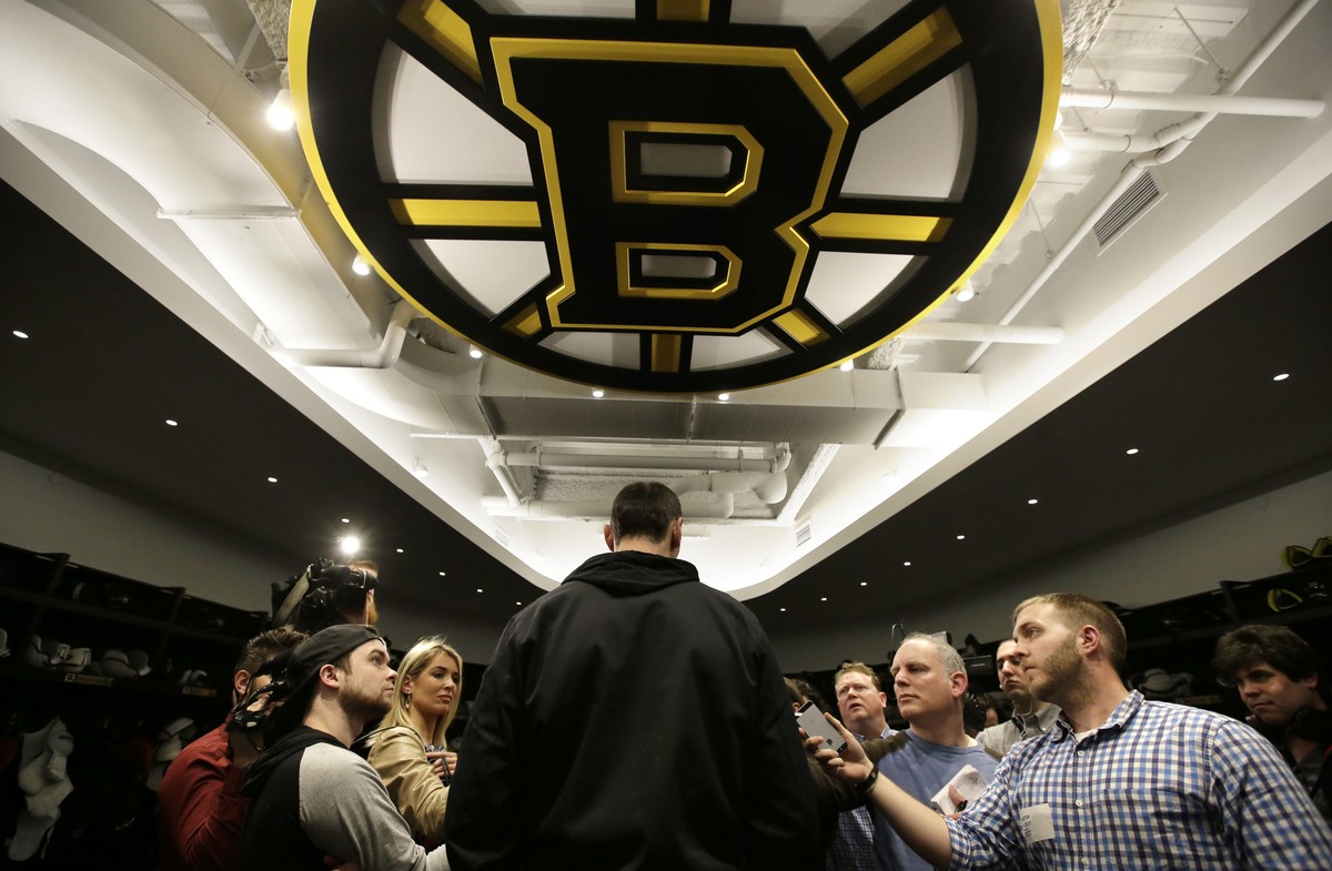 Boston Bruins defenseman Zdeno Chara, center, stands under a team emblem while taking questions from members of the media in the NHL hockey team's locker room at their training facility, Tuesday, ...