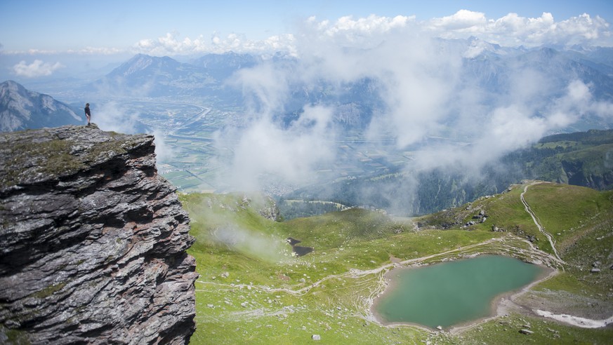 Eine Wanderin blickt von einem Felsvorsprung ueber das St. Galler und Churer Rheintal, unter ihr der Baschalvasee, auf der Fuenf Seen Wanderung, am Mittwoch, 16. Juli 2014, in Wangs-Pizol. (KEYSTONE/G ...