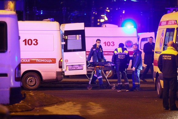 Medics transport the body of a deceased person to an ambulance near the burning building of the Crocus City Hall on the western edge of Moscow, Russia, Friday, March 22, 2024. Several gunmen have burs ...