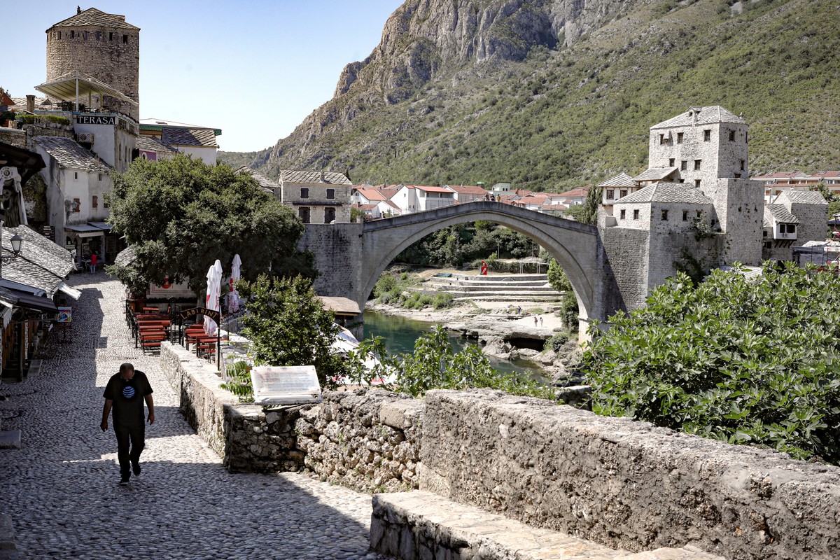 A man walks on a deserted street backdropped by the Old Bridge in Mostar, one of Bosnia's best known landmarks, Thursday, July 2, 2020. Hundreds of Bosnian tourism industry workers joined a prote ...