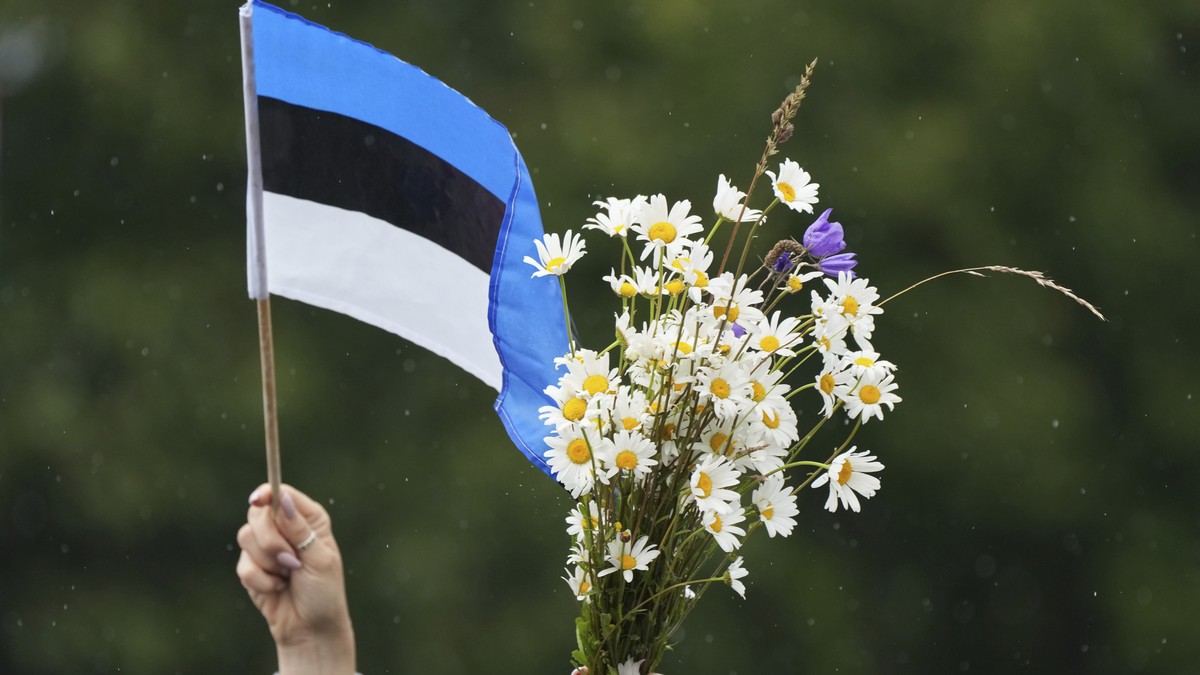 A woman waves Estonian flag and bouquet of flowers during the song festival, part of the "Iseoma" Song and Dance Celebration, at the Song Festival Grounds in Tallinn, Estonia, Sunday, July 6 ...