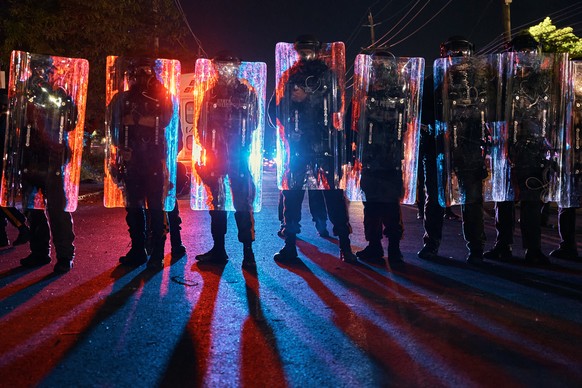 Police stand behind their shields as they prepare to clash with protesters outside the Delaney Hall detention center during a protest against the transfer of detainees and federal immigration policies ...