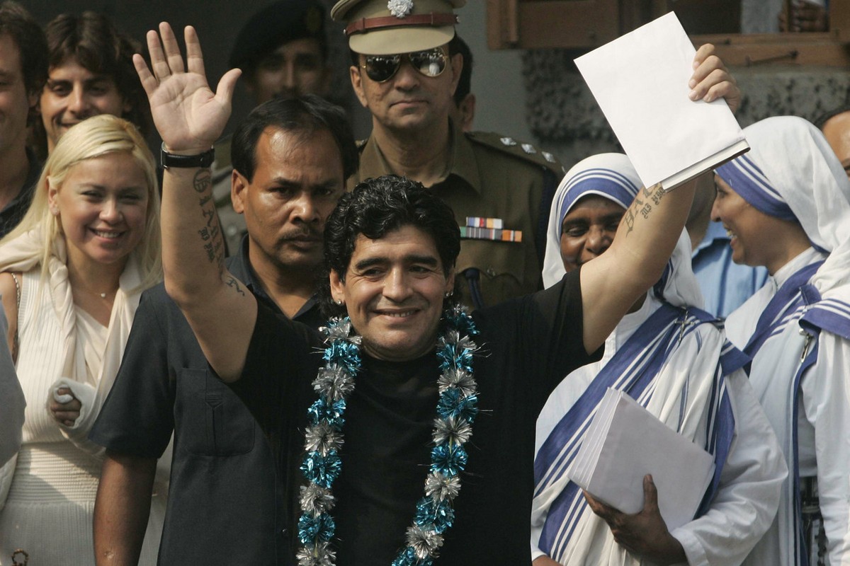 Argentina's soccer coach Diego Maradona, center, waves to the crowd as his girlfriend Veronica, left, sisters of Missionaries of Charity, right in white sarees, and security guards look on in Cal ...