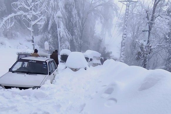 In this photo provided by the Inter Services Public Relations, people walk past vehicles trapped in a heavy snowfall-hit area in Murree, some 28 miles (45 kilometers) north of the capital of Islamabad ...