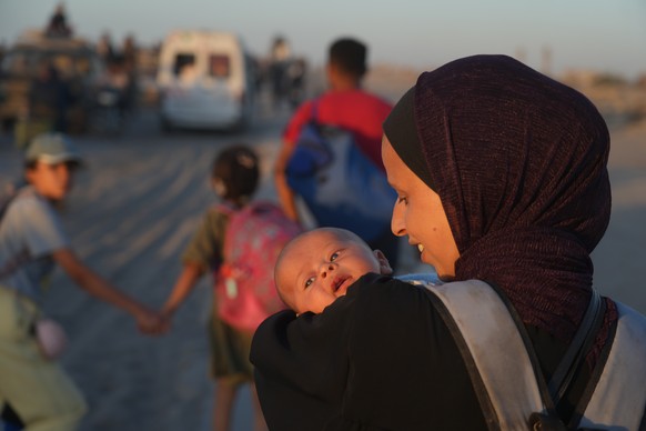 A displaced Palestinian woman carries her baby as she walks with others along the coastal road near Wadi Gaza in the central Gaza Strip, heading toward Gaza City, Friday, Oct. 10, 2025, after Israel a ...