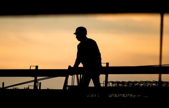 ARCHIV - 31.08.2021, Niedersachsen, Hannover: Die Silhouette eines Bauarbeiters zeichnet sich auf einer Baustelle vor dem verf