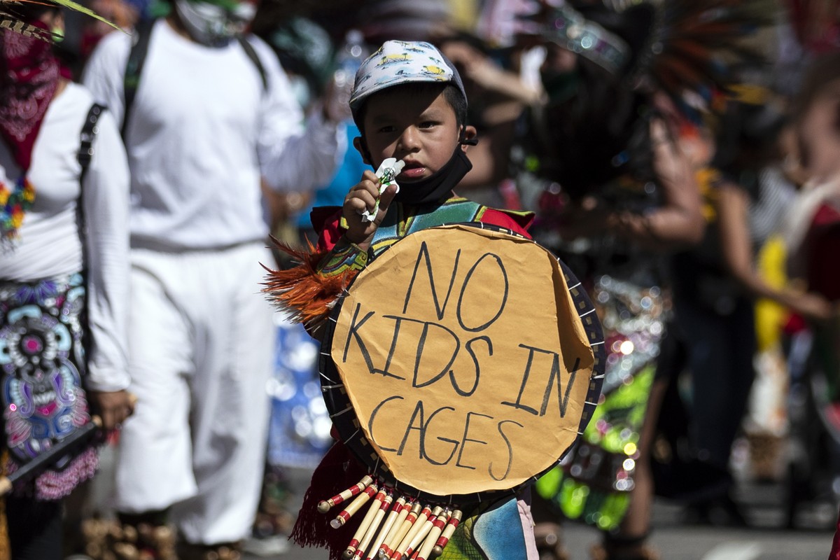 epa08542775 A young protester wearing traditional outfit holds a sign reading 'No Kids in Cages' as protesters of the Latino and indigenous community walk to take part in the Black and Brown ...