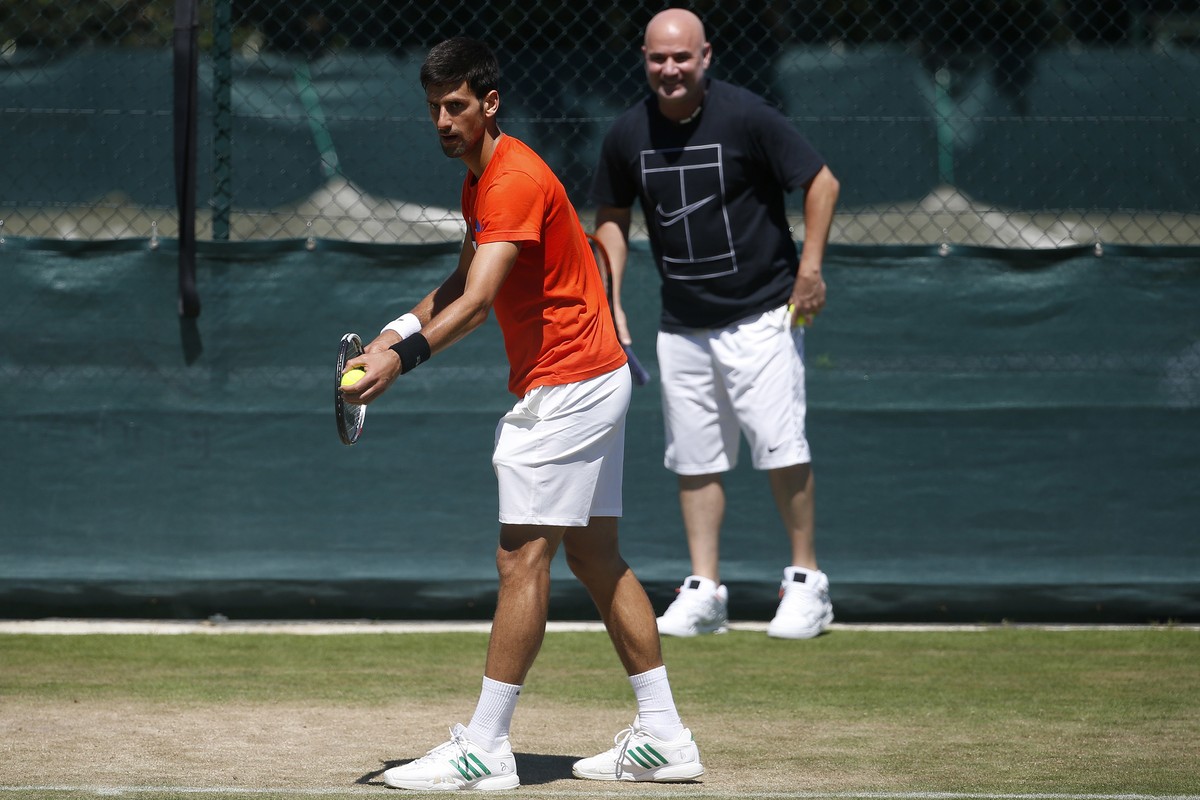 Serbia's Novak Djokovic is watched by his coach Andre Agassi as he serves during a practice session ahead of the Wimbledon Tennis Championships in London, Sunday, July 2, 2017. (AP Photo/Alastair ...