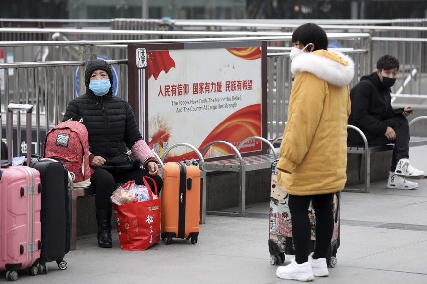 Travelers sit with their luggage outside the closed Hankou Railway Station in Wuhan in central China's Hubei Province, Thursday, Jan. 23, 2020. Overnight, Wuhan authorities announced that the air ...