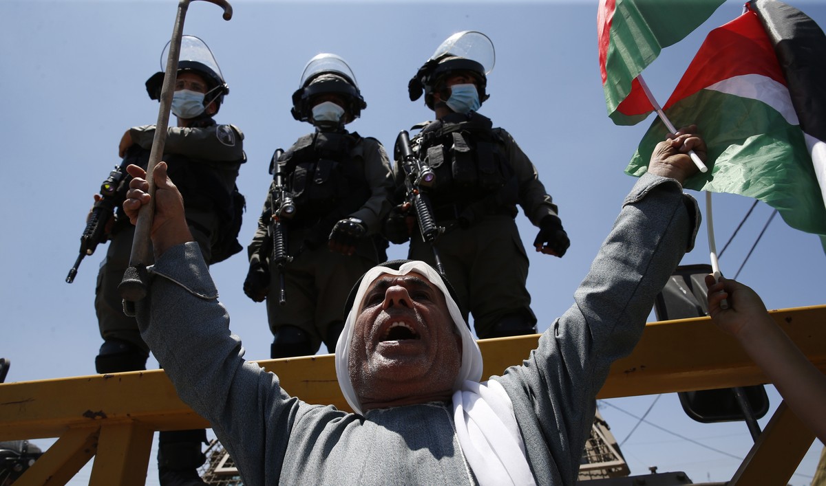 epa08564225 Palestinian protester holding Palestine's flag as he argues with Israeli soldiers as they try to reach their lands during a demonstration against Israel's plans to annex parts of ...
