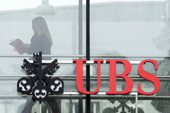 A woman walks behind a logo of Switzerland&#039;s bank UBS in Zurich, Switzerland, Tuesday, Januar 22 2018. (KEYSTONE/Ennio Leanza)