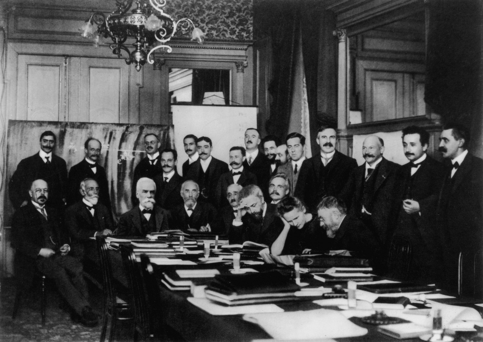 Marie Curie von Männern umgeben am Tisch sitzend während der ersten Solvay-Konferenz für Physik im Jahr 1911.