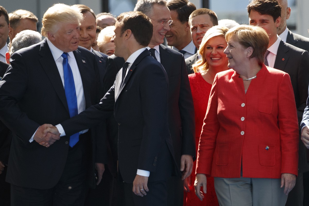 German Chancellor Angela Merkel watches as President Donald Trump shakes hands with French President Emmanuel Macron during a ceremony to unveil artifacts from the World Trade Center and Berlin Wall f ...